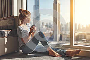 Happy young woman drinks coffee in morning at window