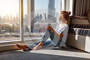 Happy young woman drinks coffee in morning at window