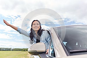 Happy young woman driving in car and waving hand