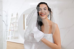 Happy young woman drying hair with towel after washing in bathroom