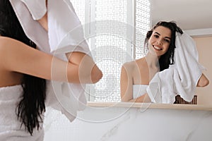 Happy woman drying hair with towel after washing near mirror in bathroom