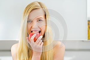 Happy young woman eating apple in kitchen