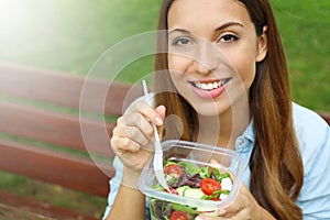 Happy young woman eating healthy salad in the park. Copy space