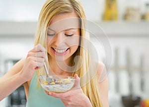 Happy young woman eating muesli in kitchen