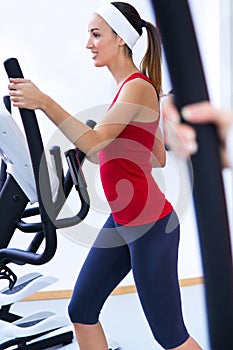 Happy young woman with elliptic machine in the gym