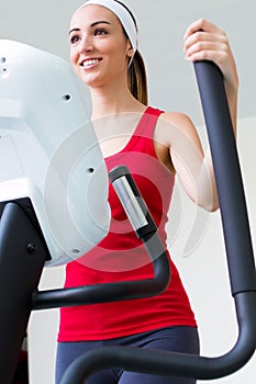 Happy young woman with elliptic machine in the gym