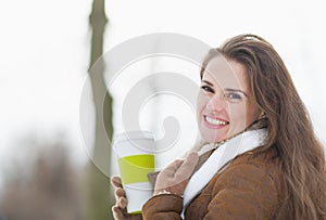 Happy young woman enjoying cup of hot beverage in winter park