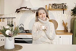 Happy young woman enjoying drinking tea or coffee in kitchen with Christmas decor over new year background