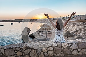 Happy young woman enjoying freedom with open hands on sea at sunset