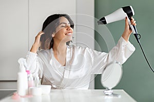Happy young woman enjoying hair drying routine, home interior