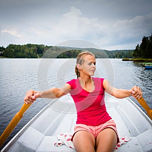 Happy, young woman enjoying rowing boat ride on a lake