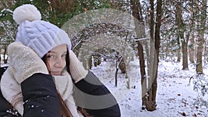 Happy young woman enjoying a snowy day in the winter park, wearing white hat and gloves