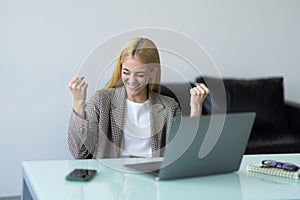 Happy young woman excited with great news, win, success, luck. Woman looking at laptop screen making winner gesture, shouting fir