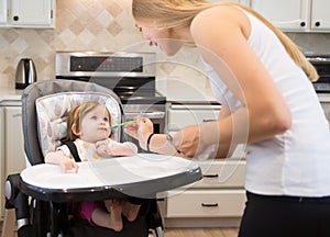 Happy young woman feeding cute little girl with a spoon.