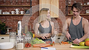 Happy young woman feeding her boyfriend with paprika pepper while he cutting vegetables for salad. Healthy eating, diet