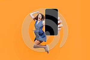 Happy young woman flying and jumping in air and showing big mobile empty screen