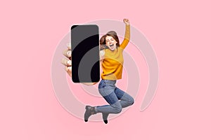 Happy young woman flying and jumping in air and showing big mobile empty screen