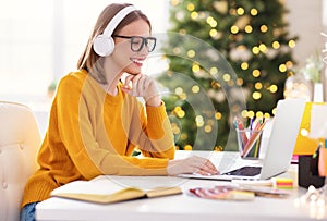 Happy young woman freelancer in headphones working remote at laptop at home before Christmas