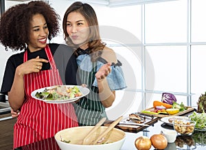 Happy young woman friends different races make salad together and show holding salad on plate