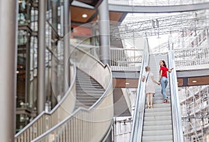 Young woman friends on escalator in shopping mall