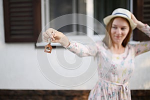 Happy young woman in front of a new house with the keys to a new house, focus on the keys.The concept of real estate