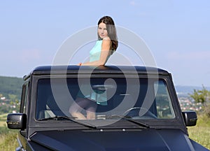 Happy young woman getting out the car's sunroof