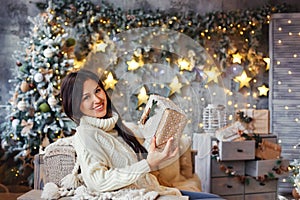 Happy young woman with a gift on Christmas eve in a beautifully decorated room with bokeh lights
