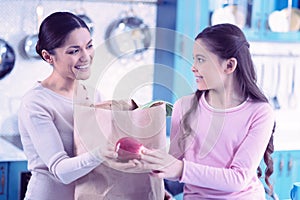 Happy young woman giving red apple to child and looking friendly