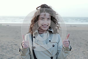 Happy young woman giving a thumbs up while standing on a beach