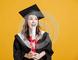 Happy young woman in graduation gowns holding diploma and looking away