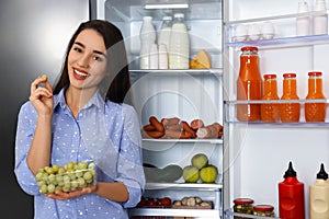 Happy young woman with grape near open refrigerator