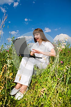 Happy Young Woman on the grass field with a laptop