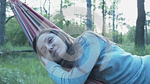 Happy young woman on a hammock. Smiling beautiful girl relaxes in nature, lying on a hammock.