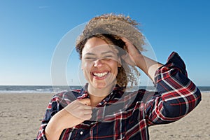 Happy young woman with hand in curly hair at the beach