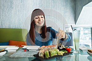 Happy young woman, having a dinner in chinese restaurant, eating sushi, looking at a plate with rolls and taking tasty