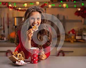 Happy young woman having eating christmas cookies in kitchen