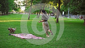 Happy, young woman having fun with her dog outdoors - running, chasing it around plaid with picnic on grass