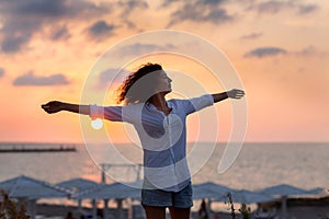 Happy young woman having fun with open hands at the sunset on sea.