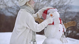 Happy young woman having fun in winter. Snowman and funny girl. Make a Snow man.