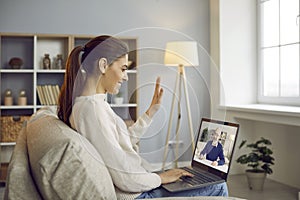 Happy young woman having online meeting , smiling and waving hello at laptop screen