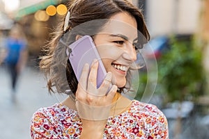 Happy young woman having remote conversation talking on smartphone, good news gossip in city street