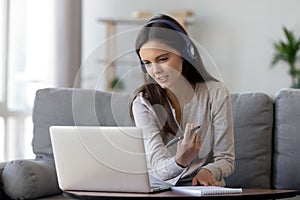 Happy young woman in headphones speaking looking at laptop