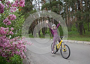 Happy young woman in a helmet joyfully raises her hands to ride a bike