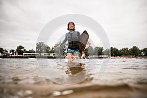Happy young woman with helmet and wakeboarding board runs out of the water