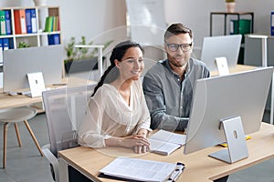 Happy young woman and her male colleague working together, using modern computer in open space office
