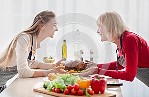 Happy young woman and her senior mother serving table with traditional festive turkey, having family holiday celebration