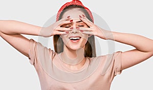 Happy young woman hiding her face with fingers, covering her eye. Pretty female covering her face by hand wearing beige t-shirt,