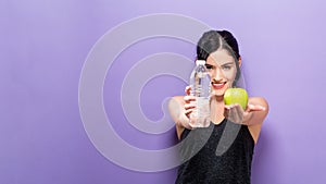 Happy young woman holding apple and water