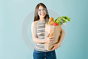 Happy young woman is holding a bag of groceries with vegetables