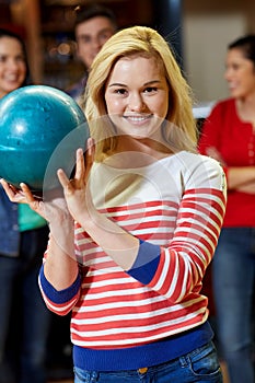 Happy young woman holding ball in bowling club